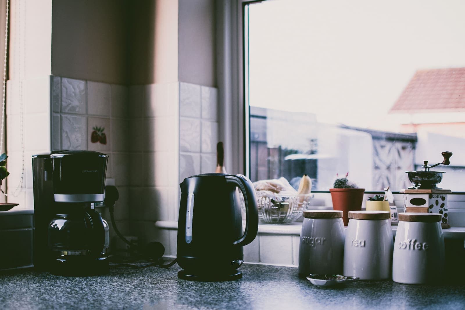 A kitchen counter beside a window with storage canisters and a kettle in daylight
