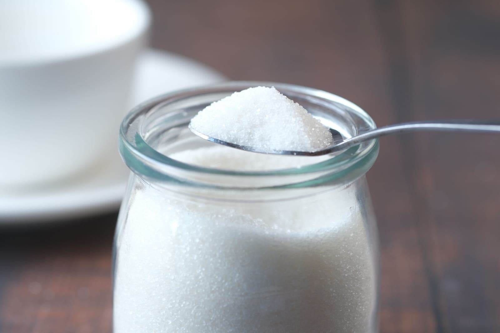 A jar of sugar water with a spoon on a bright surface
