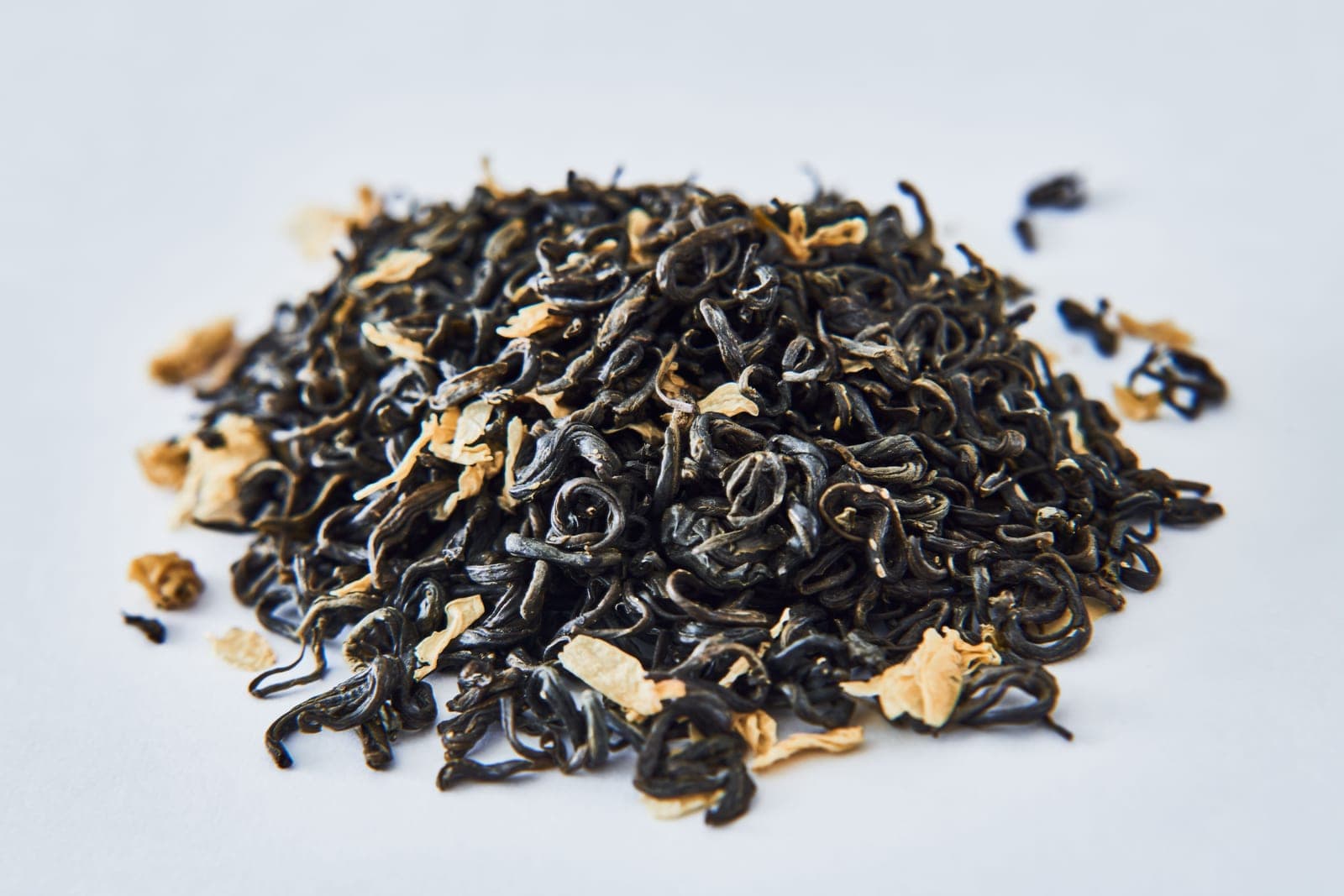 Loose black tea leaves with dried petals photographed close up on a white background