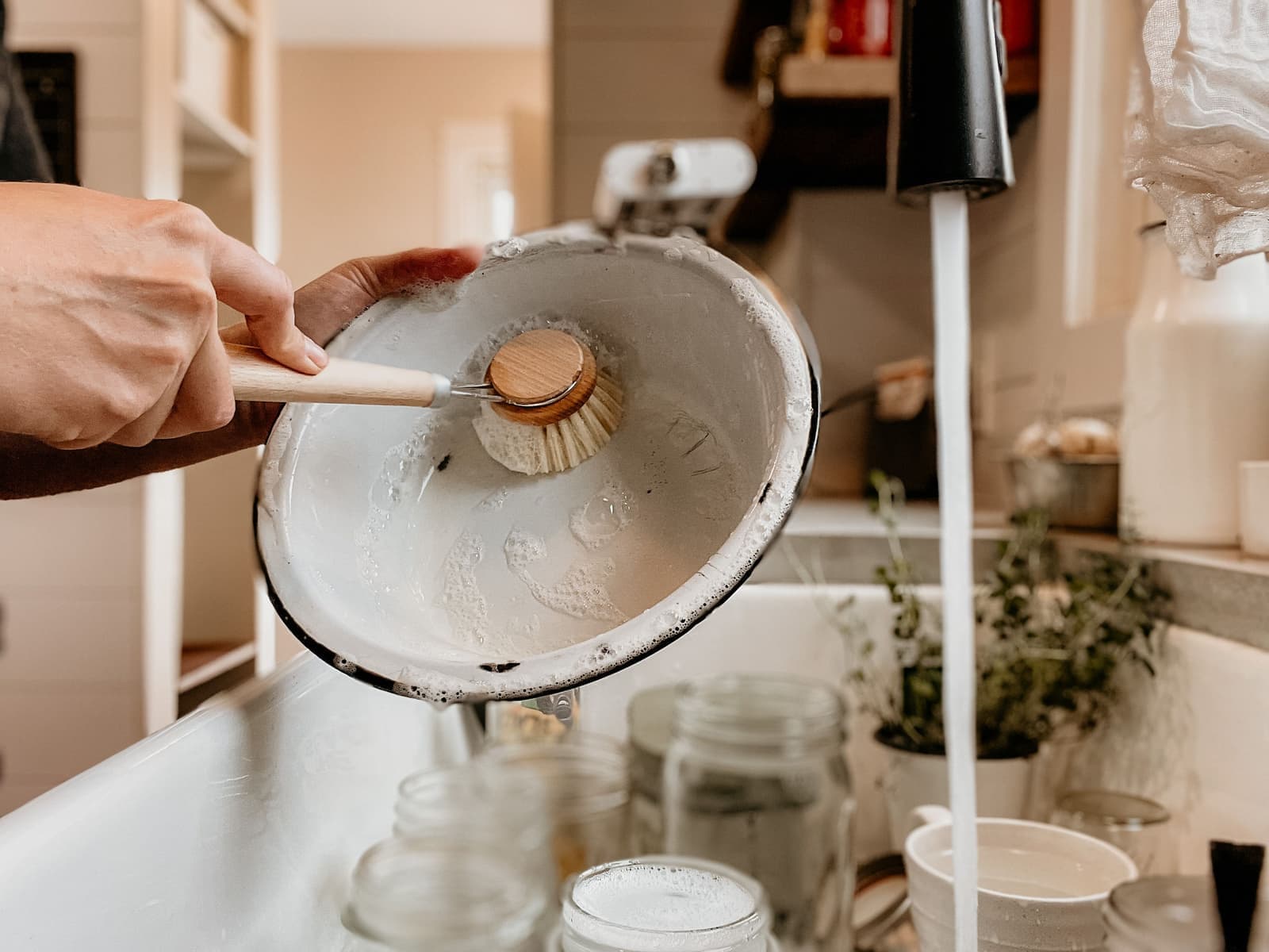 A glass jar being washed under running water in a sink