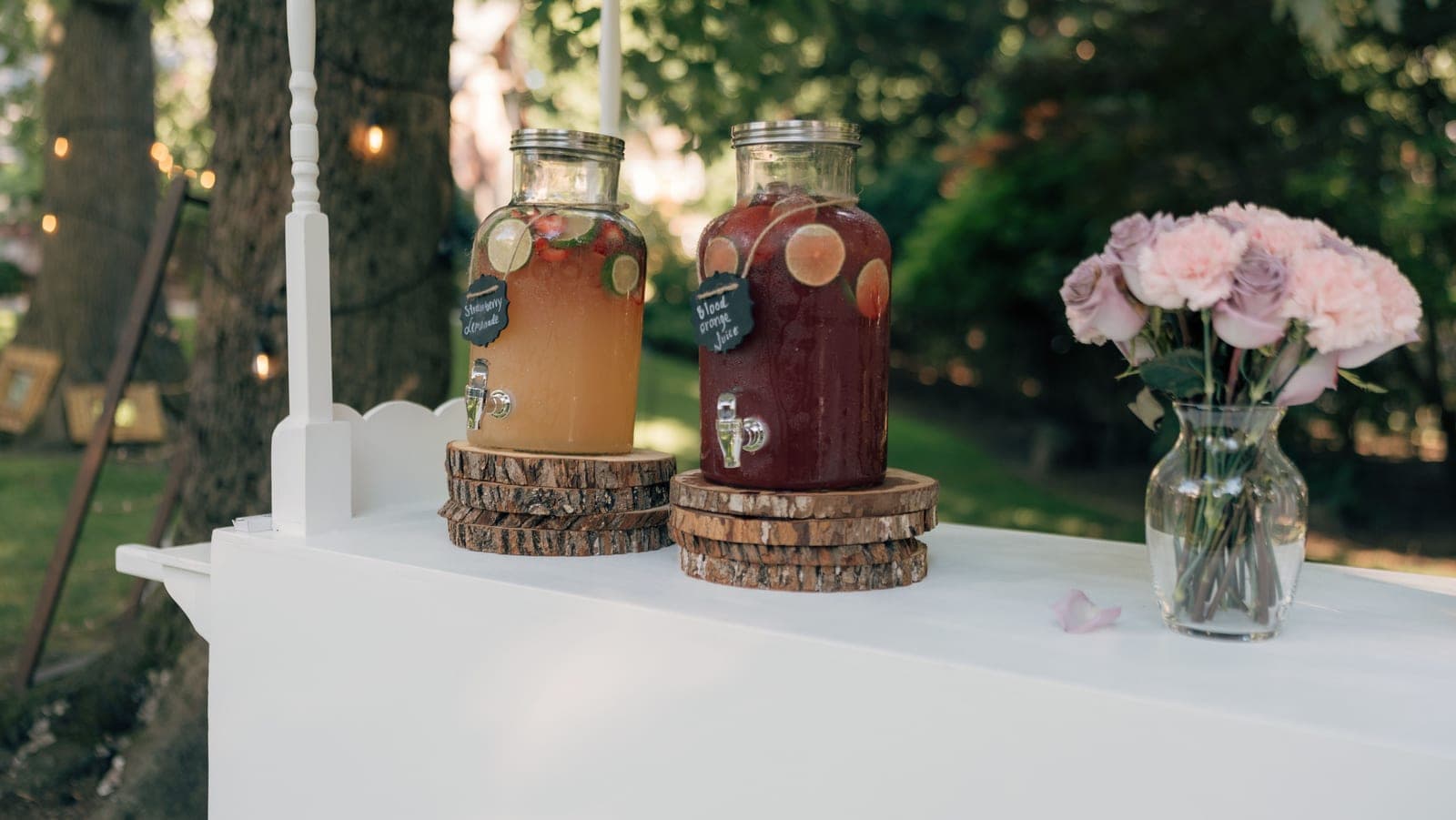 Two glass drink dispensers with spigots on a white table in bright daylight