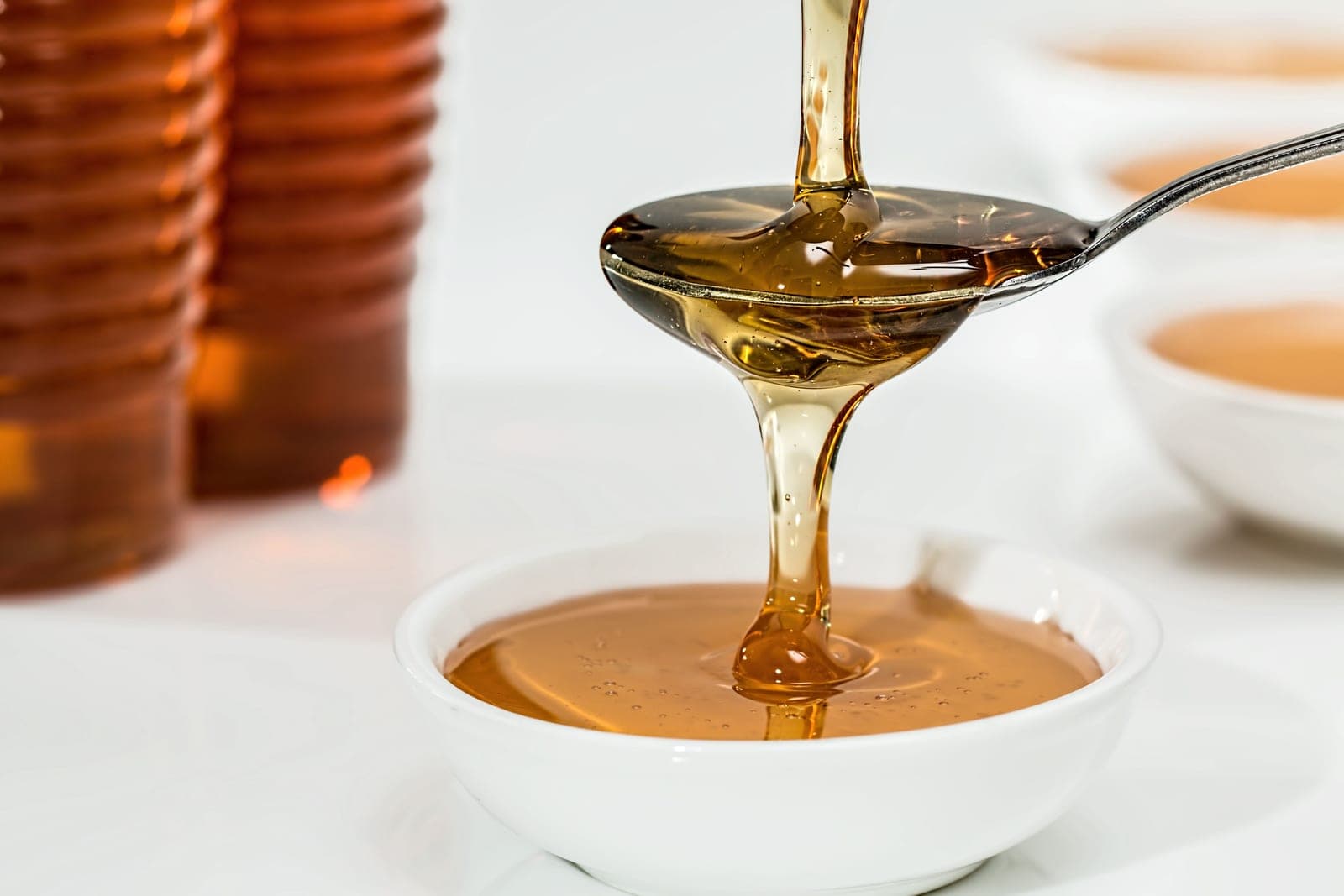 Honey pouring slowly from a spoon into a white bowl in bright light