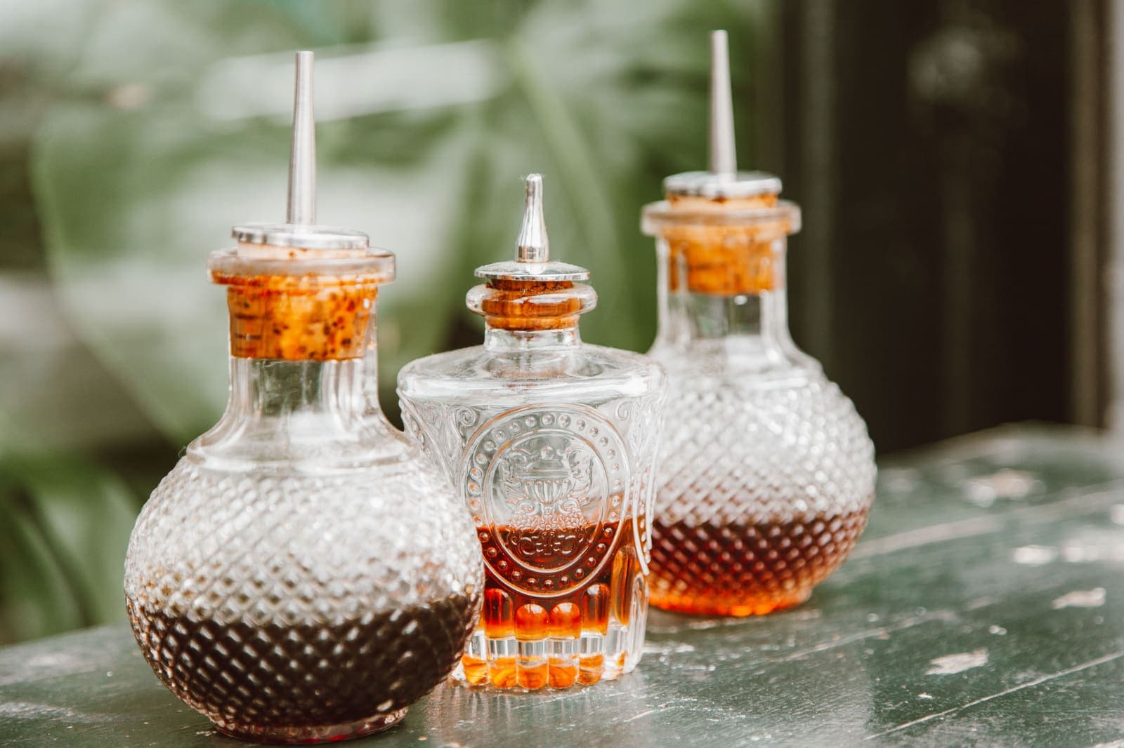 Three vintage glass condiment bottles holding dark liquid on a rustic table