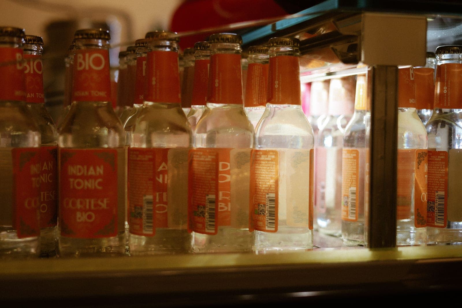 Glass bottles of a clear drink arranged upright on a refrigerator shelf