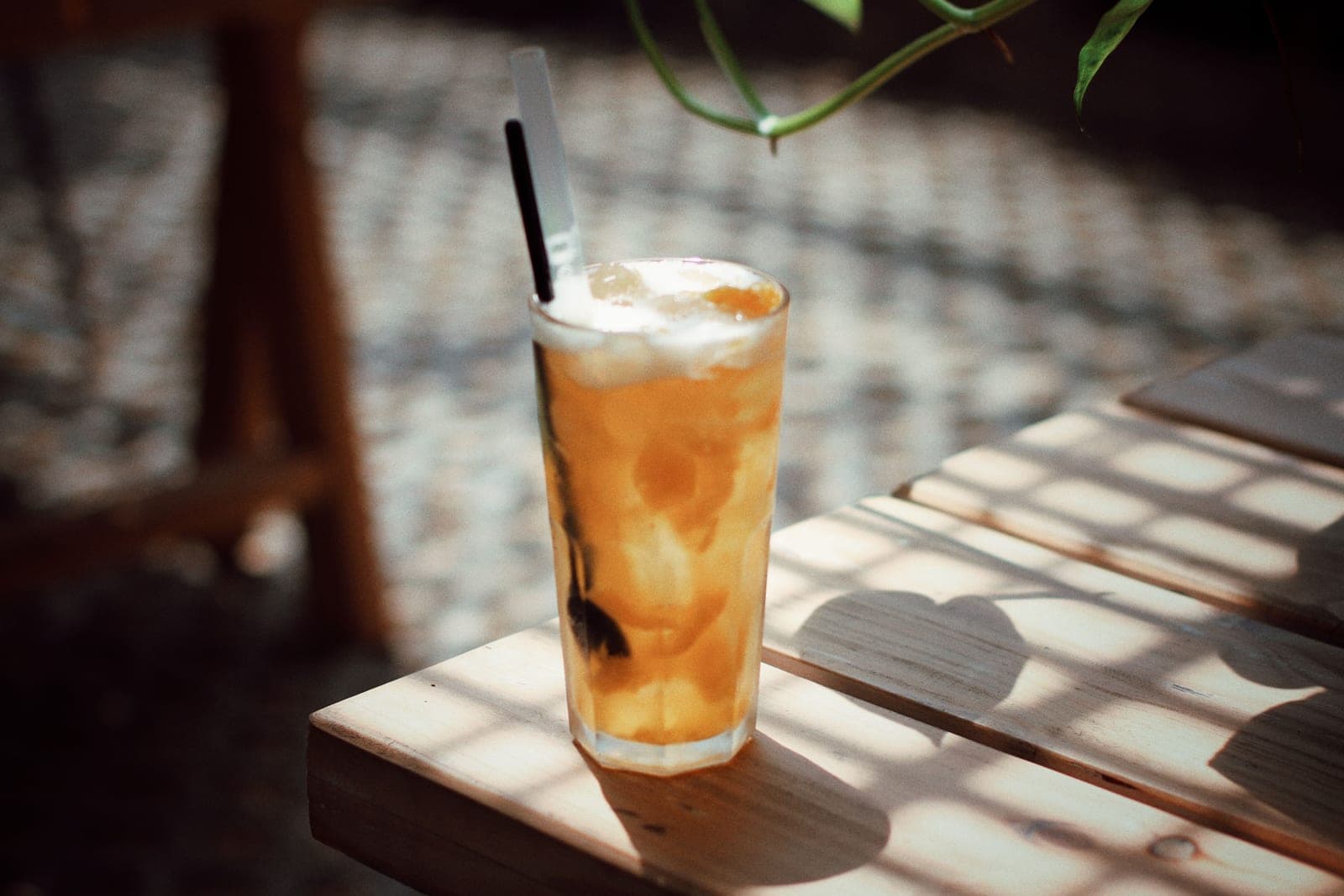 A tall glass of iced tea catching sunlight on a wooden table